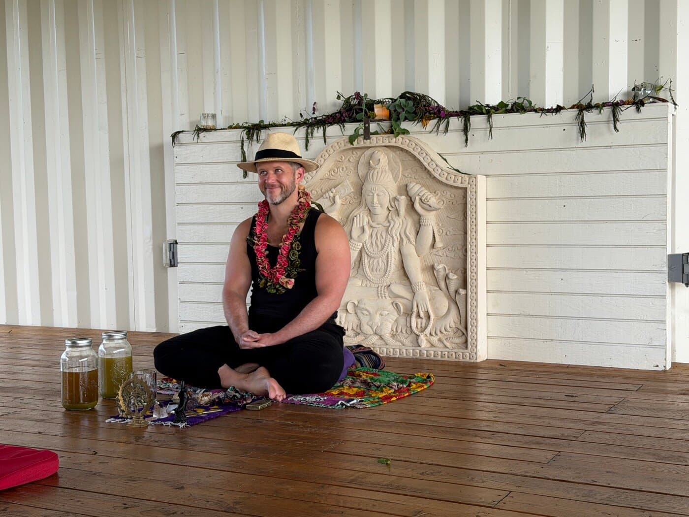 Sacred Ways guide seated cross-legged at a Hawaiian altar, marigold lei and offerings before him