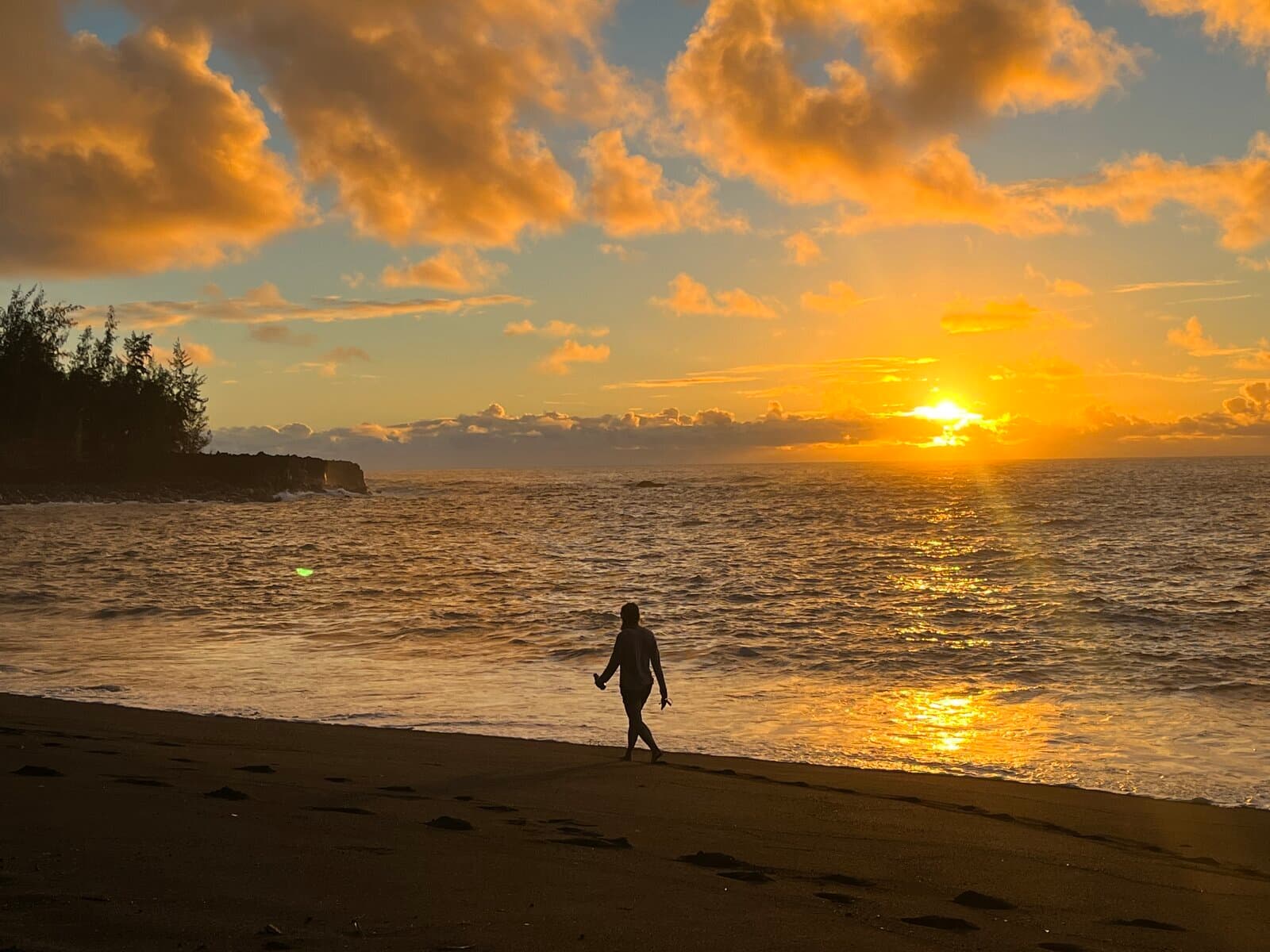 Solitary figure walking on a Big Island beach at sunset, dramatic sky